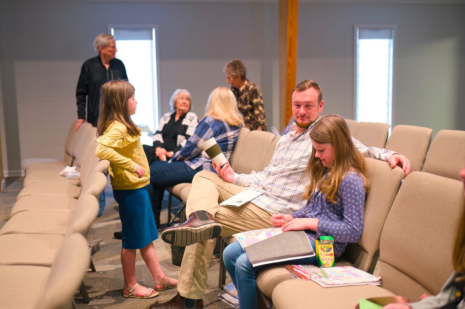 A man and a young girl seated together in the sanctuary before the service, coloring with crayons.