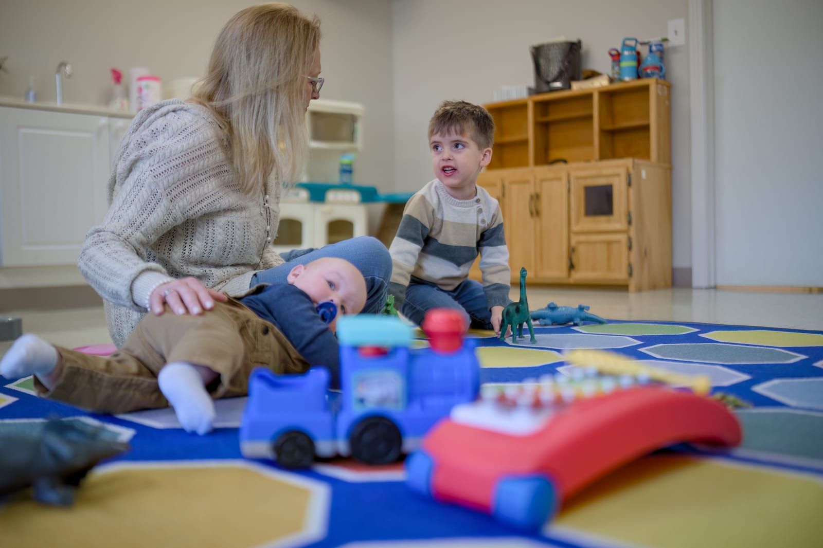A caregiver sitting on the floor with a baby and a toddler during nursery care at Lucy Baptist Church.