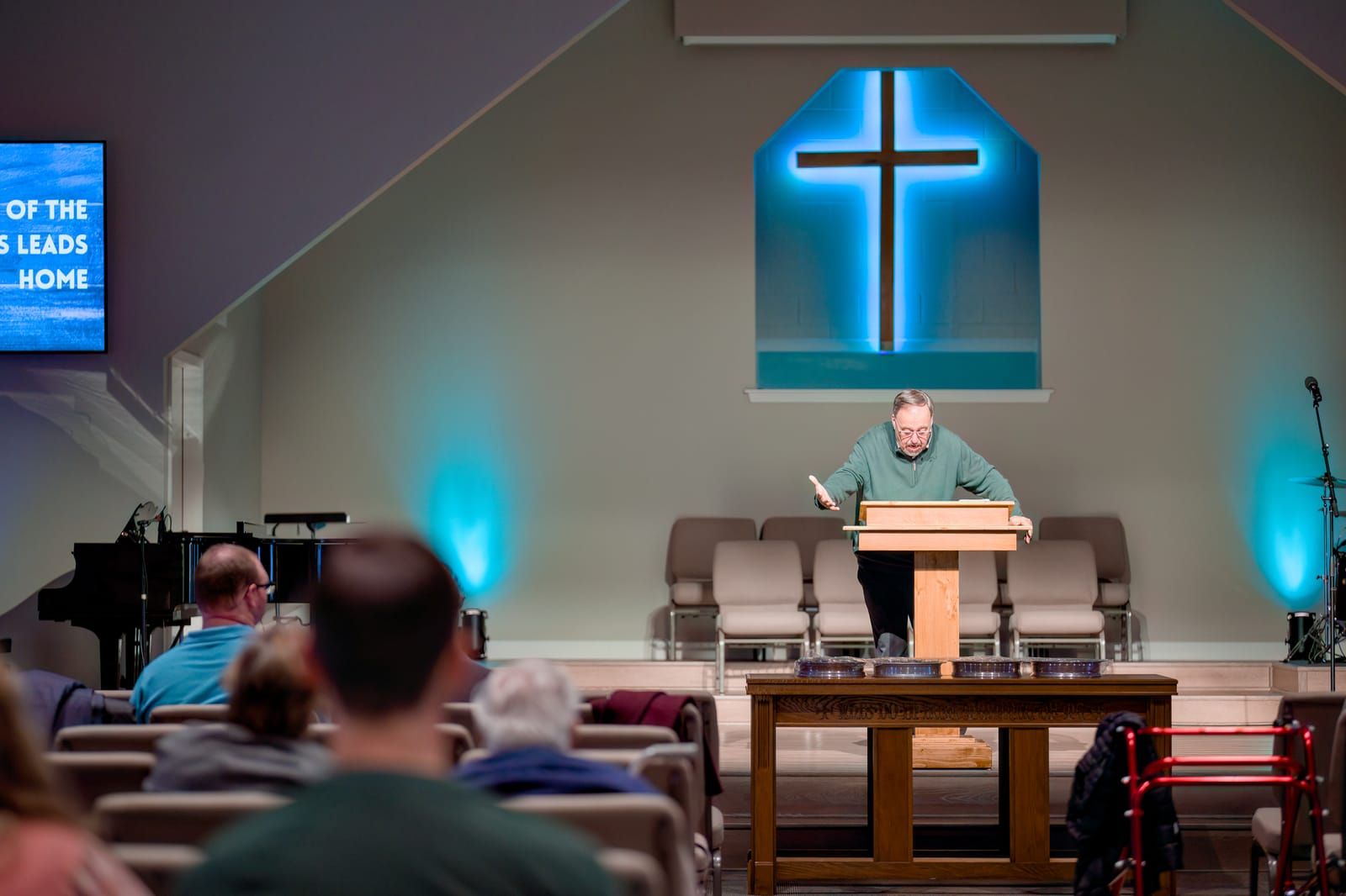 Pastor preaching from the wooden pulpit with an open Bible, the congregation seated in the foreground.